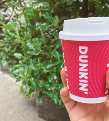 A person holding up a Dunkin' coffee cup