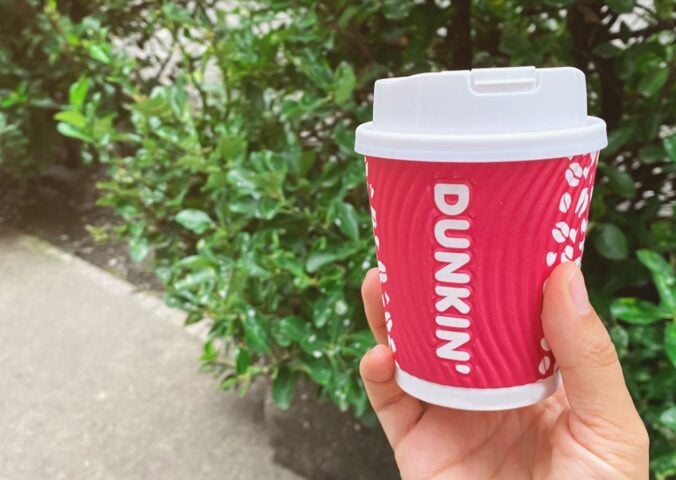 A person holding up a Dunkin' coffee cup