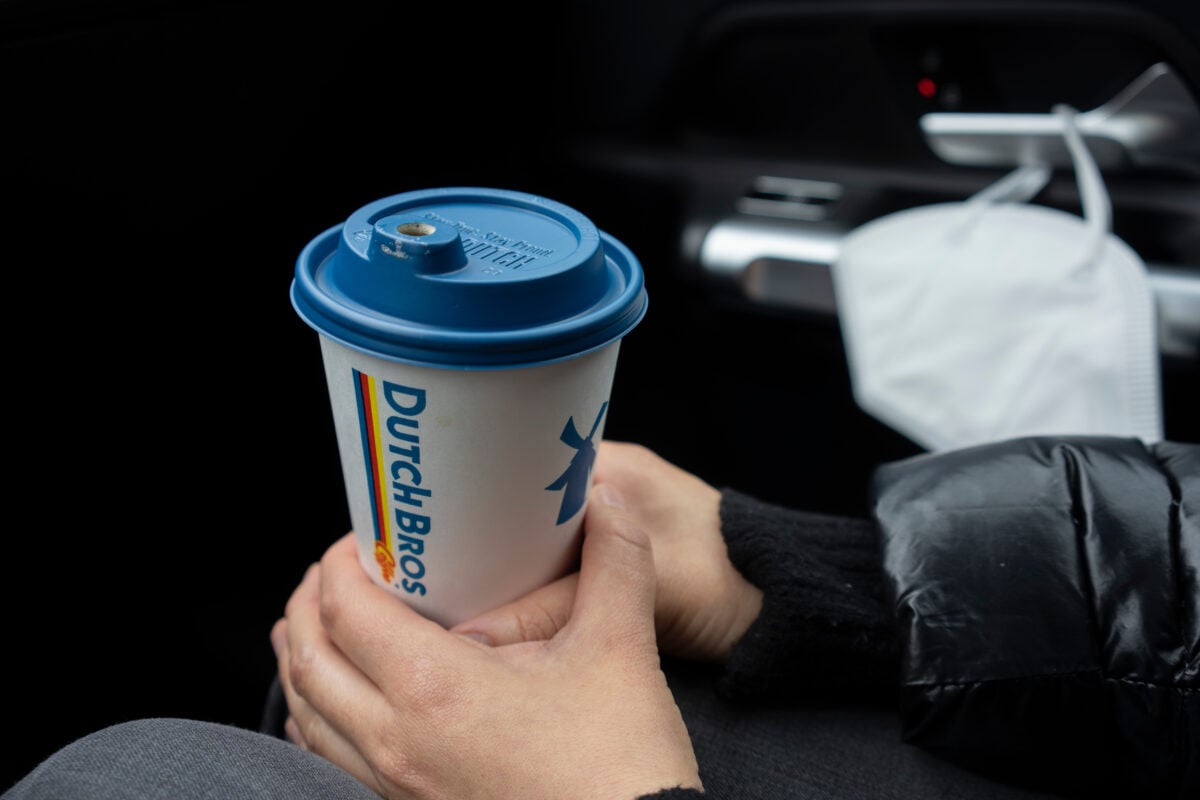 Photo shows someone's hands holding a Dutch Bros coffee cup in a car