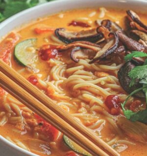 a bowl of ginger noodle & vegetable red curry soup made with zucchini, mushrooms, and coconut milk