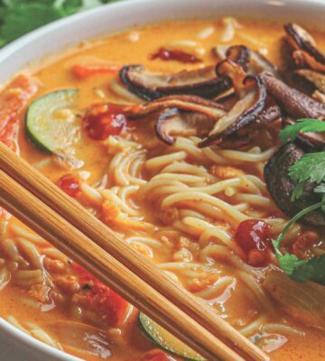 a bowl of ginger noodle & vegetable red curry soup made with zucchini, mushrooms, and coconut milk