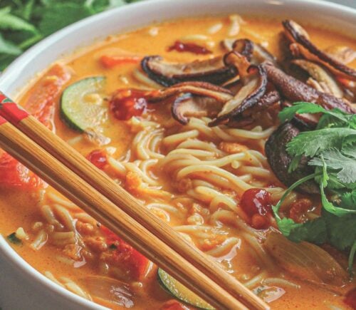 a bowl of ginger noodle & vegetable red curry soup made with zucchini, mushrooms, and coconut milk