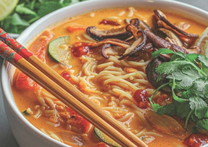 a bowl of ginger noodle & vegetable red curry soup made with zucchini, mushrooms, and coconut milk