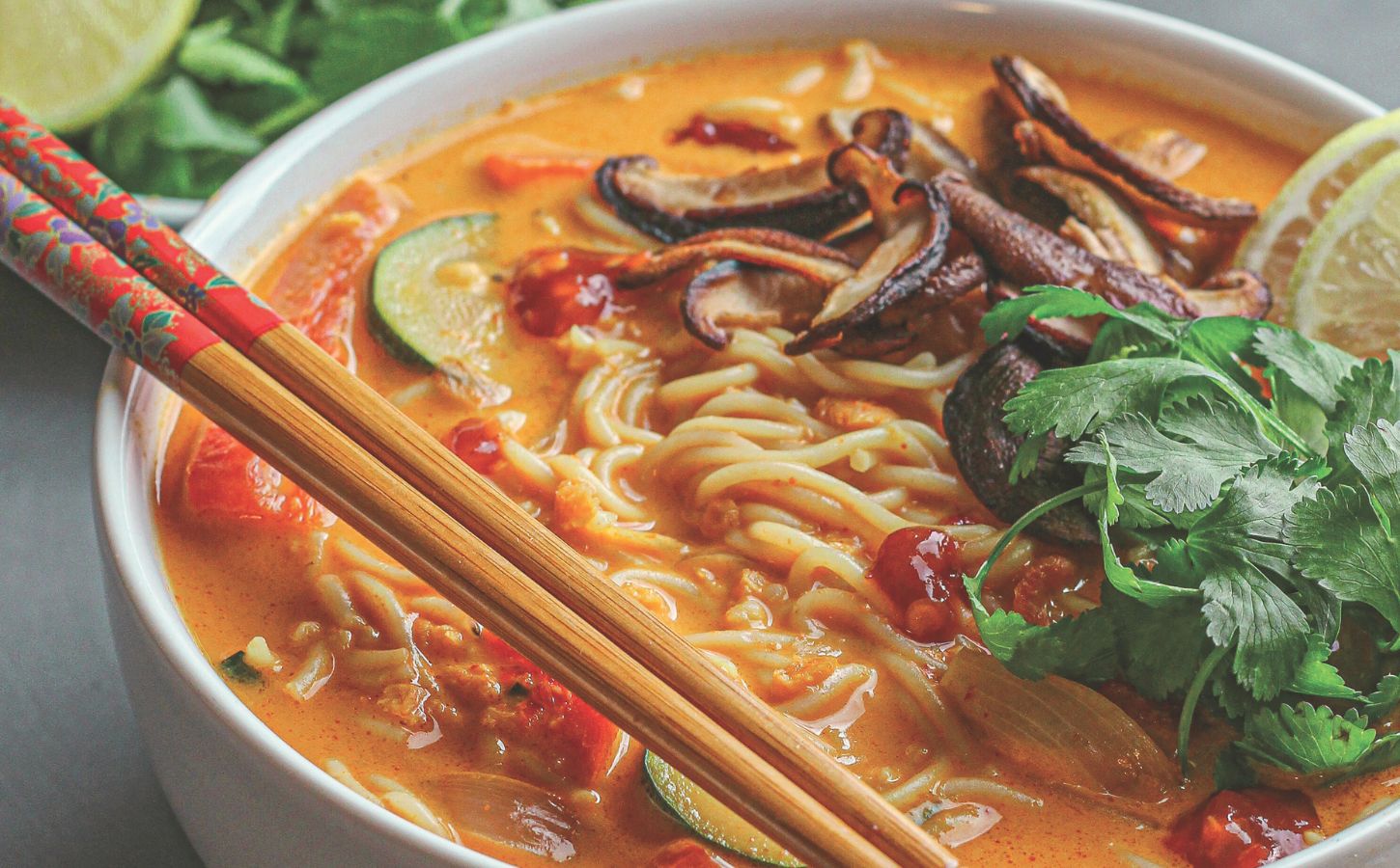 a bowl of ginger noodle & vegetable red curry soup made with zucchini, mushrooms, and coconut milk