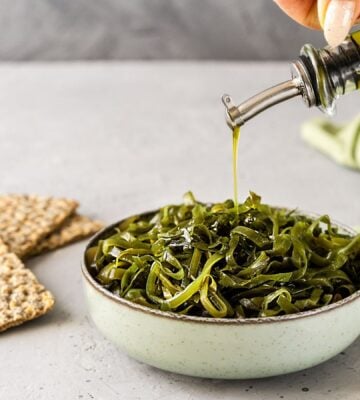 Photo shows a bowl of seaweed as someone drizzles olive oil over the top