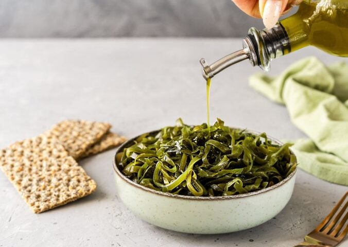 Photo shows a bowl of seaweed as someone drizzles olive oil over the top