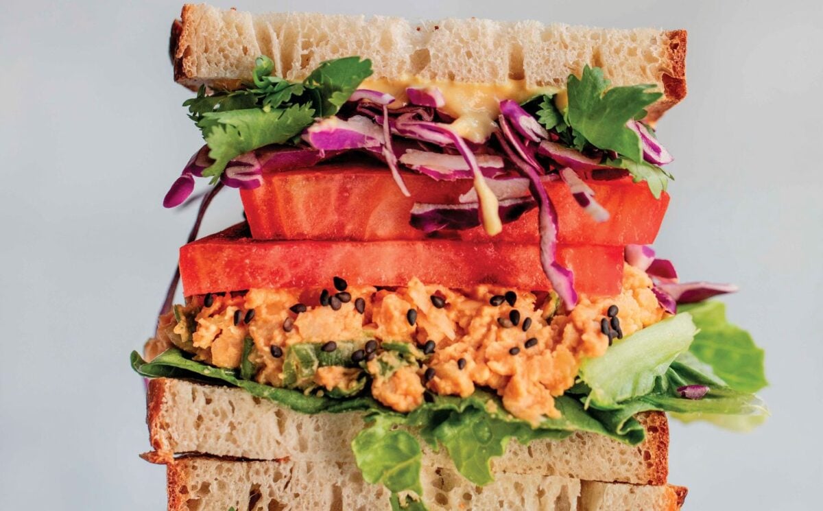 a picture of stacked peanut miso chickpea salad sandwiches with sesame, tomato, chickpea spread, and greens, part of the high protein vegan recipes to make for Veganuary