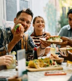 Photo shows a group of young people sat around a table at a Mexican restaurant eating tacos