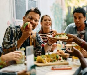 Photo shows a group of young people sat around a table at a Mexican restaurant eating tacos