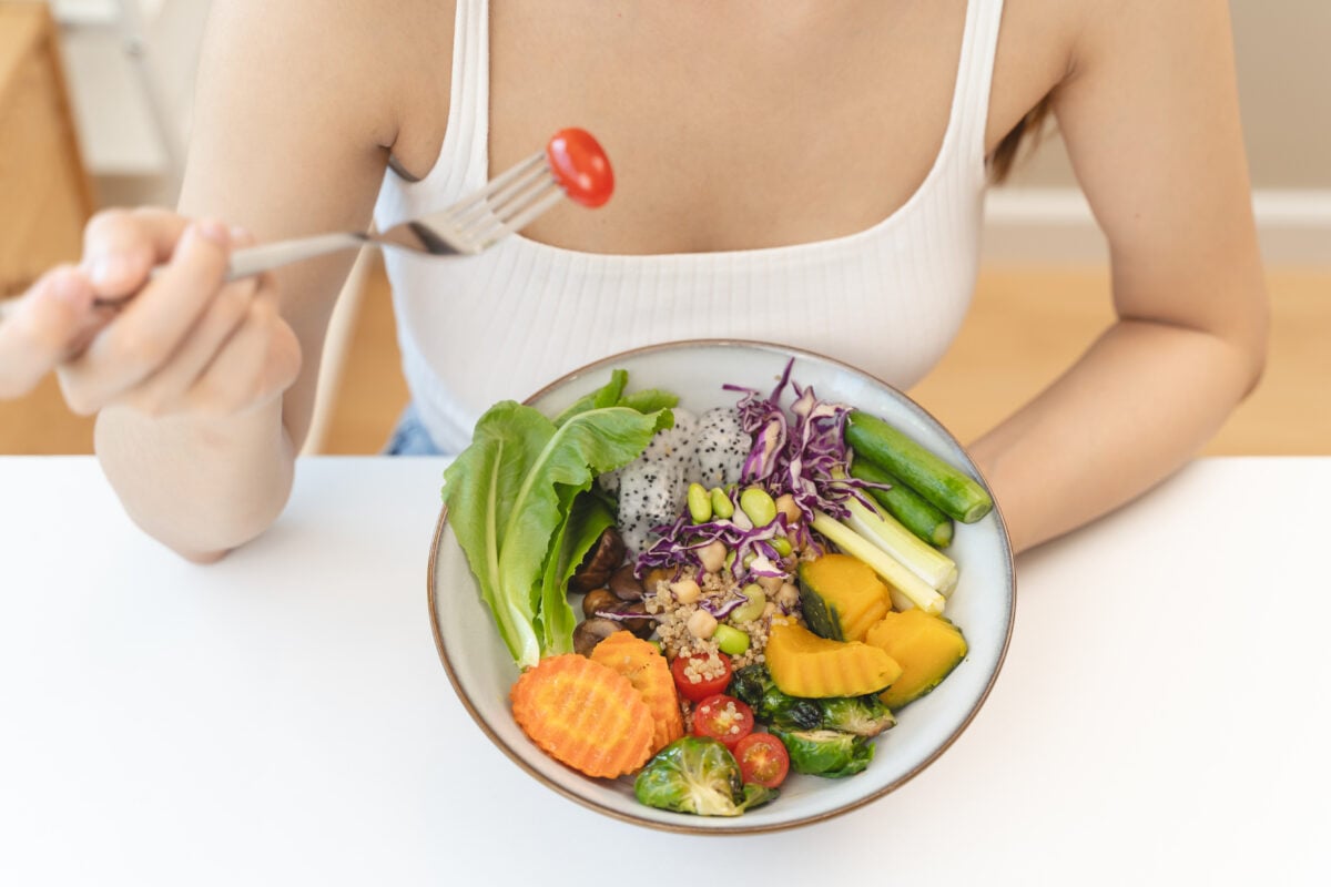 Photo shows someone eating a colorful bowl of food including fresh salad and vegetables