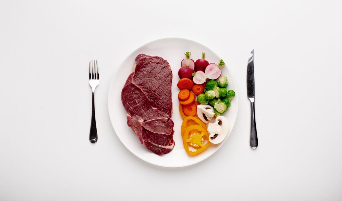 Photo shows a white plate with a raw steak on one side and raw vegetables on the other