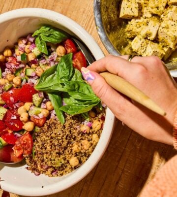 A quinoa bowl filled with chickpeas, tomatoes, cucumber, and basil, next to some dairy-free tofu feta