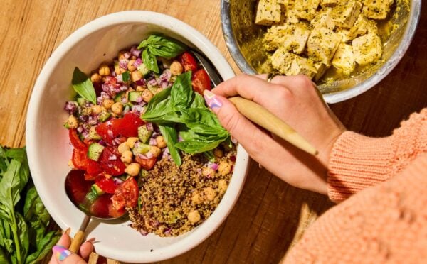 A quinoa bowl filled with chickpeas, tomatoes, cucumber, and basil, next to some dairy-free tofu feta