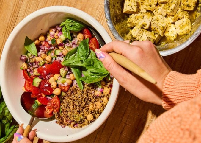 A quinoa bowl filled with chickpeas, tomatoes, cucumber, and basil, next to some dairy-free tofu feta