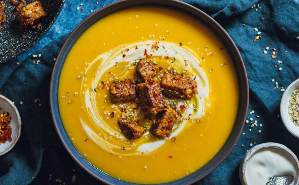 a bowl of spicy swede soup with ginger topped with vegan yogurt, chili, and tempeh chunks