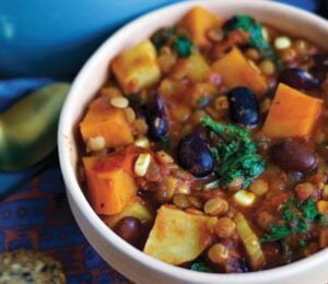 a bowl of sweet potato and kale chili with avocado, corn, kidney beans, and lentils