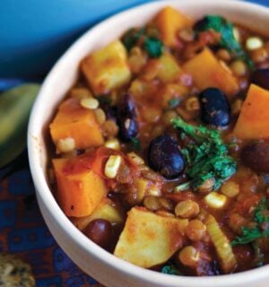 a bowl of sweet potato and kale chili with avocado, corn, kidney beans, and lentils