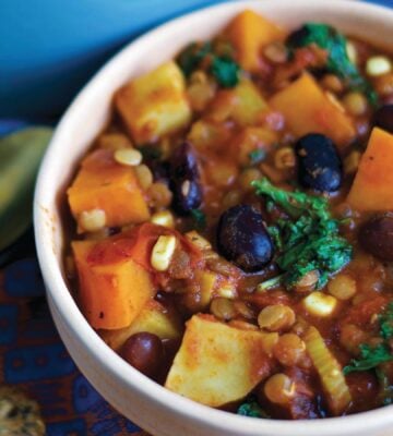 a bowl of sweet potato and kale chili with avocado, corn, kidney beans, and lentils