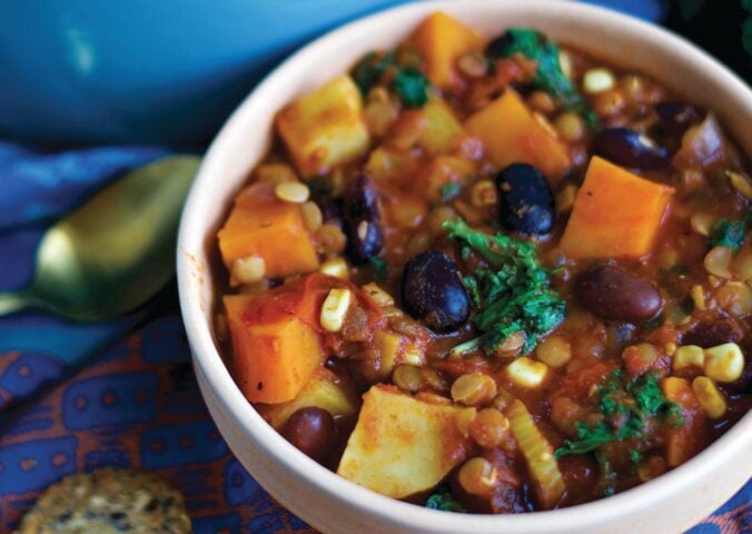 a bowl of sweet potato and kale chili with avocado, corn, kidney beans, and lentils