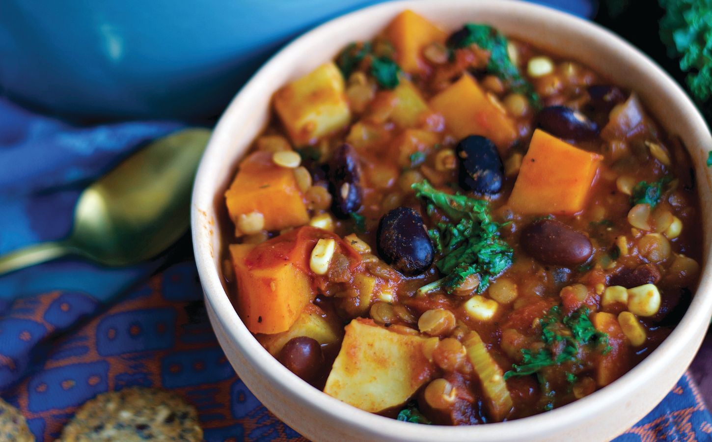 a bowl of sweet potato and kale chili with avocado, corn, kidney beans, and lentils