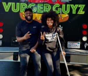 Photo shows Tabitha Brown and Vurger Guyz founder Na’eem Outler sat on the back of the Vurger Guyz food truck