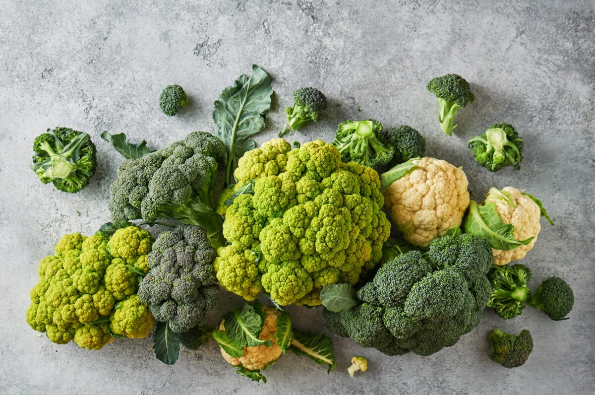 Photo shows a pile of broccoli and cauliflower, both of the family brassica, on a grey table