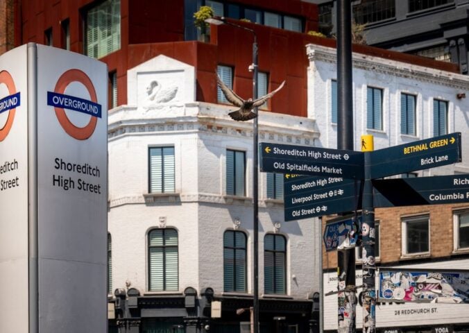 An sign for the Shoreditch High Street Overground station next to some signs in the Hackney borough