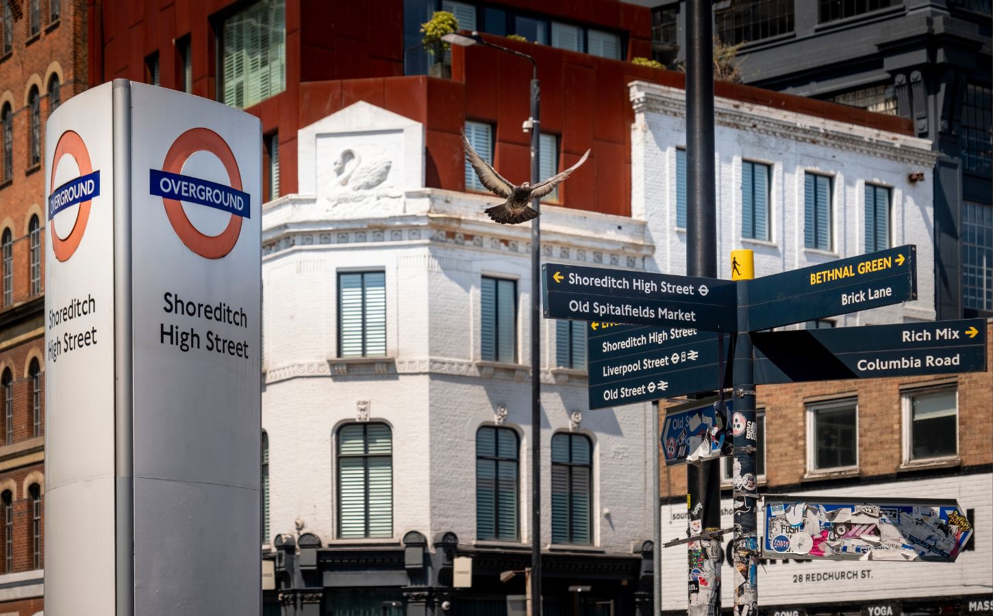 An sign for the Shoreditch High Street Overground station next to some signs in the Hackney borough