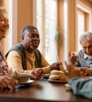 Photo shows a group of older people sat around a table eating and laughing together