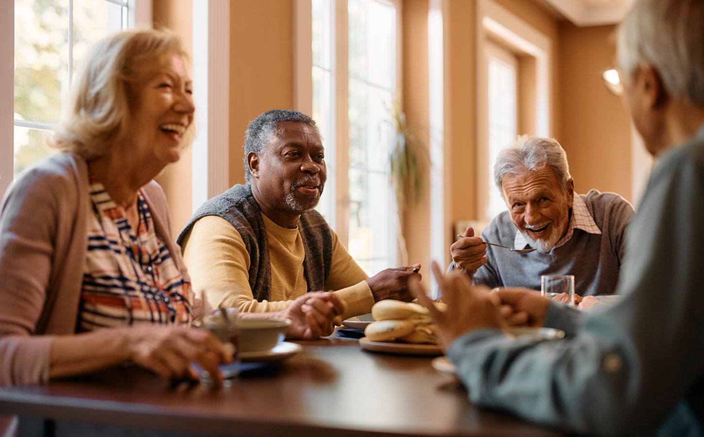 Photo shows a group of older people sat around a table eating and laughing together