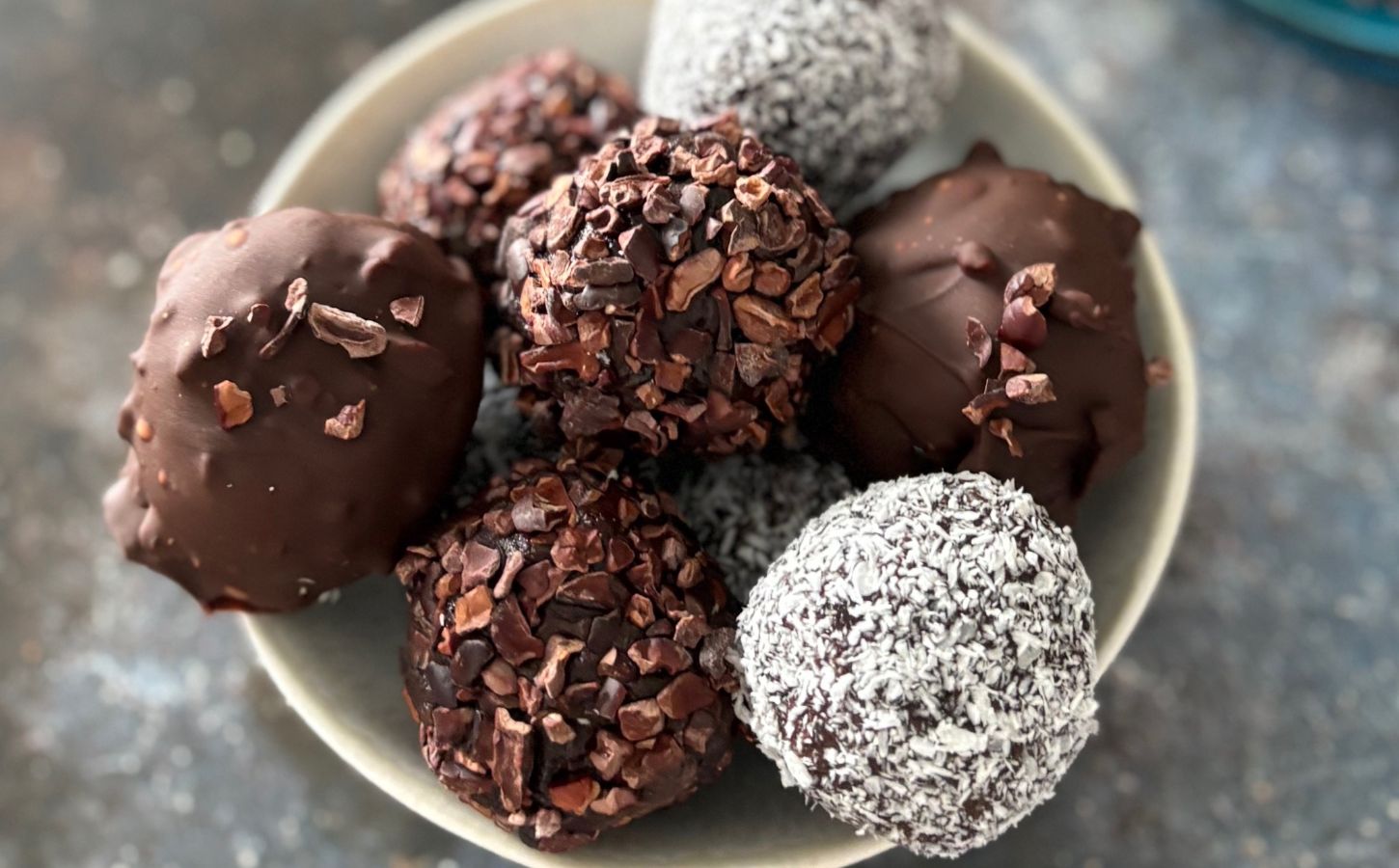 a picture of a bowl of vegan zero waste cake pops that are covered in chocolate, coconut, and cocoa nibs