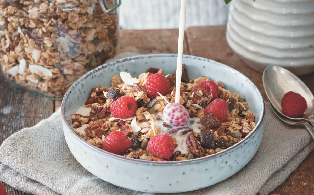 a bowl of vegan cinnamon and pecan granola with raspberries