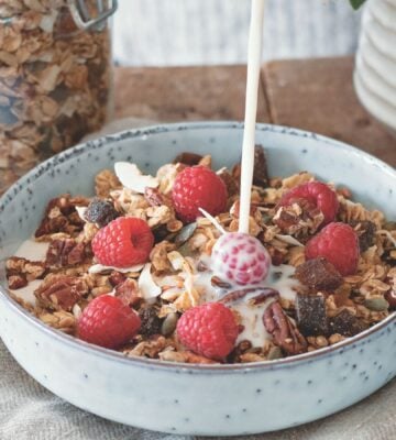 a bowl of vegan cinnamon and pecan granola with raspberries