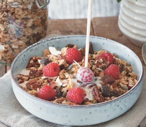 a bowl of vegan cinnamon and pecan granola with raspberries