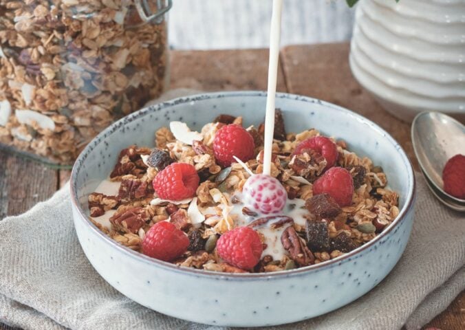 a bowl of vegan cinnamon and pecan granola with raspberries