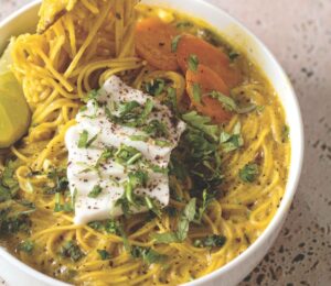 a bowl of vegan creamy coconut curry ramen with carrot, soft tofu, lime, and herbs