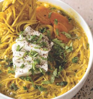 a bowl of vegan creamy coconut curry ramen with carrot, soft tofu, lime, and herbs