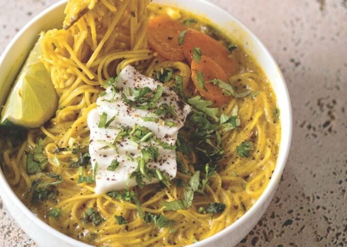 a bowl of vegan creamy coconut curry ramen with carrot, soft tofu, lime, and herbs