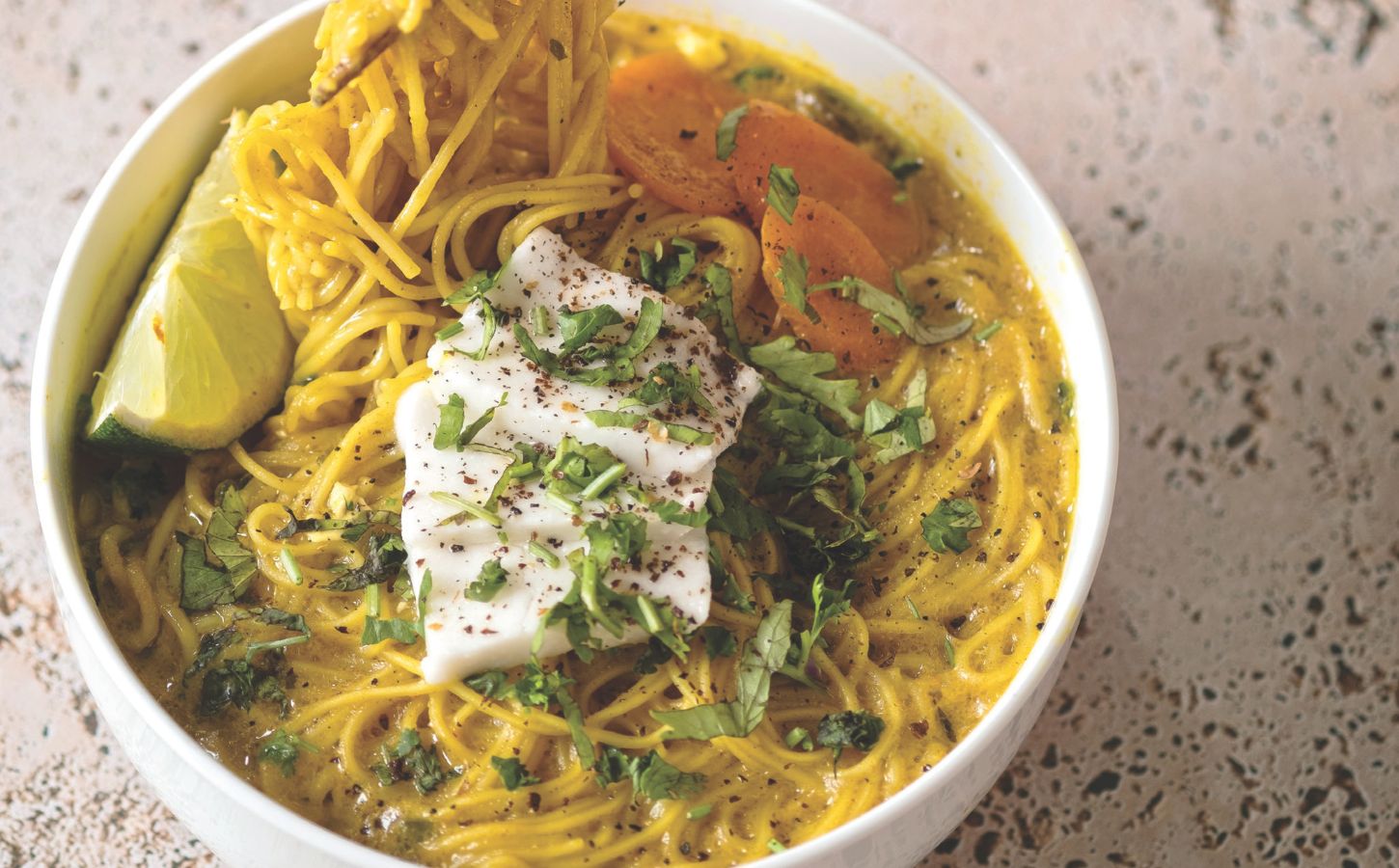 a bowl of vegan creamy coconut curry ramen with carrot, soft tofu, lime, and herbs