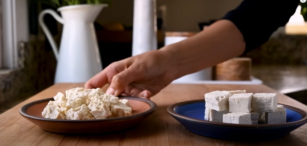 Two plates of raw tofu, one cut up in blocks and the other broken into chunks