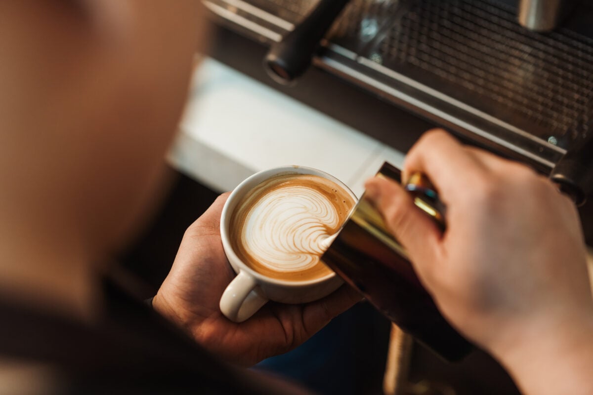 Photo shows someone pouring foamed milk into a cup of coffee