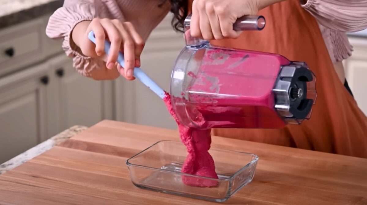 Nisha Vora pouring bright pink homemade beet hummus from a blender into a glass food container