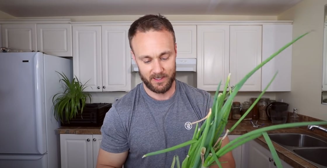 Plant-based nutritionist Derek Simnett holding green onions for a video on vegan food hacks