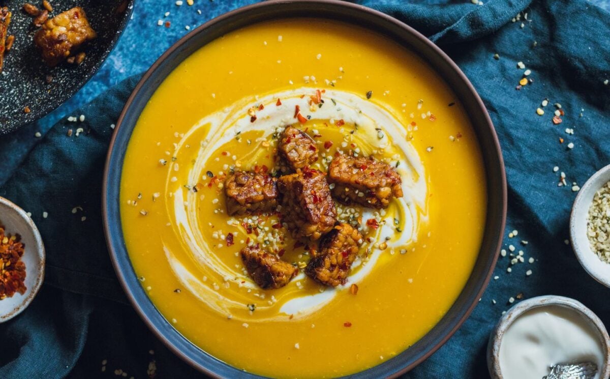 a bowl of spicy swede soup with ginger topped with vegan yogurt, chili, and tempeh chunks part of spicy vegan dinner recipes