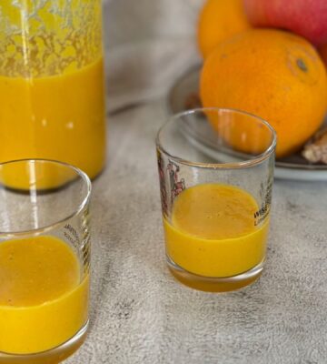 Two ginger and turmeric shots next to oranges and apples