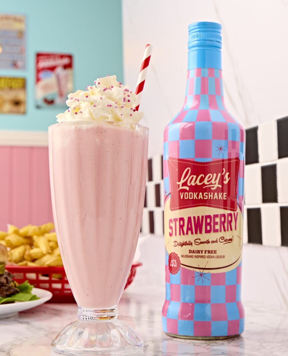 Photo shows a bottle of the strawberry flavor Lacey's Vodkashakes on a countertop in an 1950s-style American diner, next to a milkshake topped with whipped cream, fries, and a burger