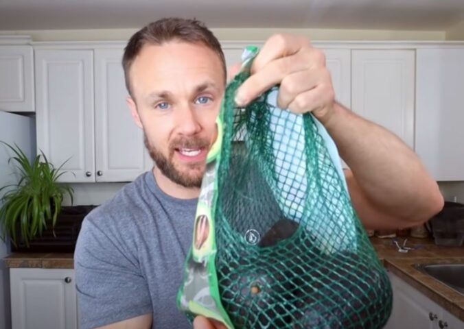 Plant-based nutritionist Derek Simnett holding up a pack of avocados for a video on vegan food hacks