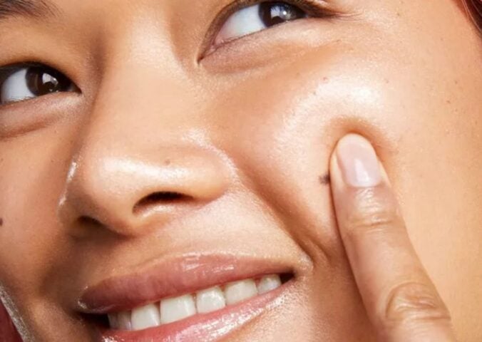 A woman applying vegan glass skin serum in an advert for BYOMA