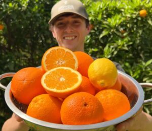 Vegan homesteader Luke Kelsall holding up a tub of oranges that he grew himself