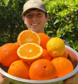 Vegan homesteader Luke Kelsall holding up a tub of oranges that he grew himself